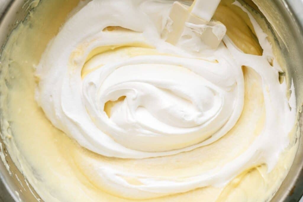 Cool whip folded into banana pudding in a glass mixing bowl.