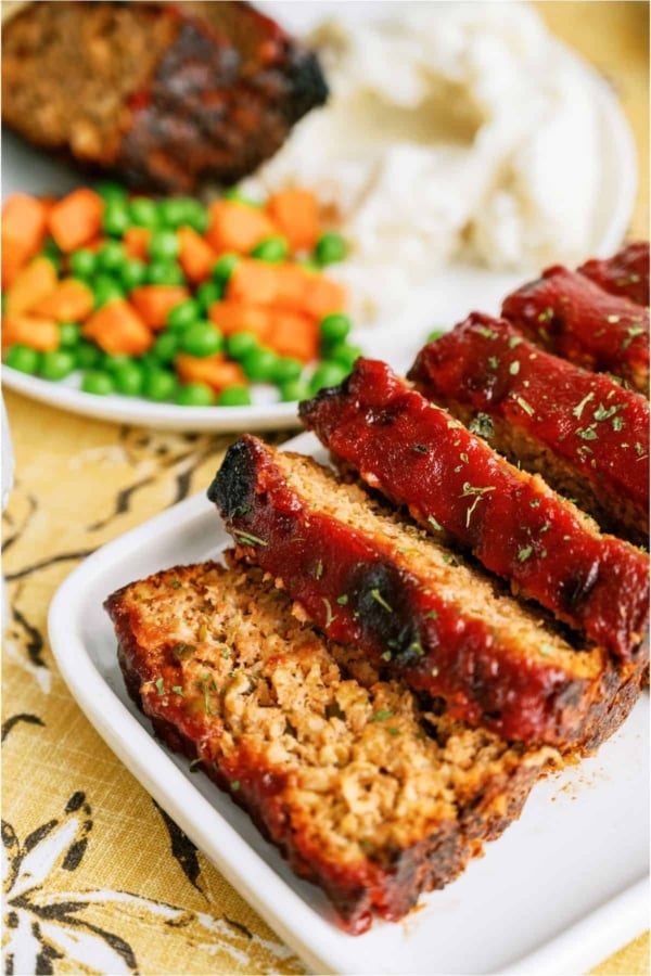 Easy Turkey Meatloaf on a serving platter sliced with a plate of vegetables in the background.