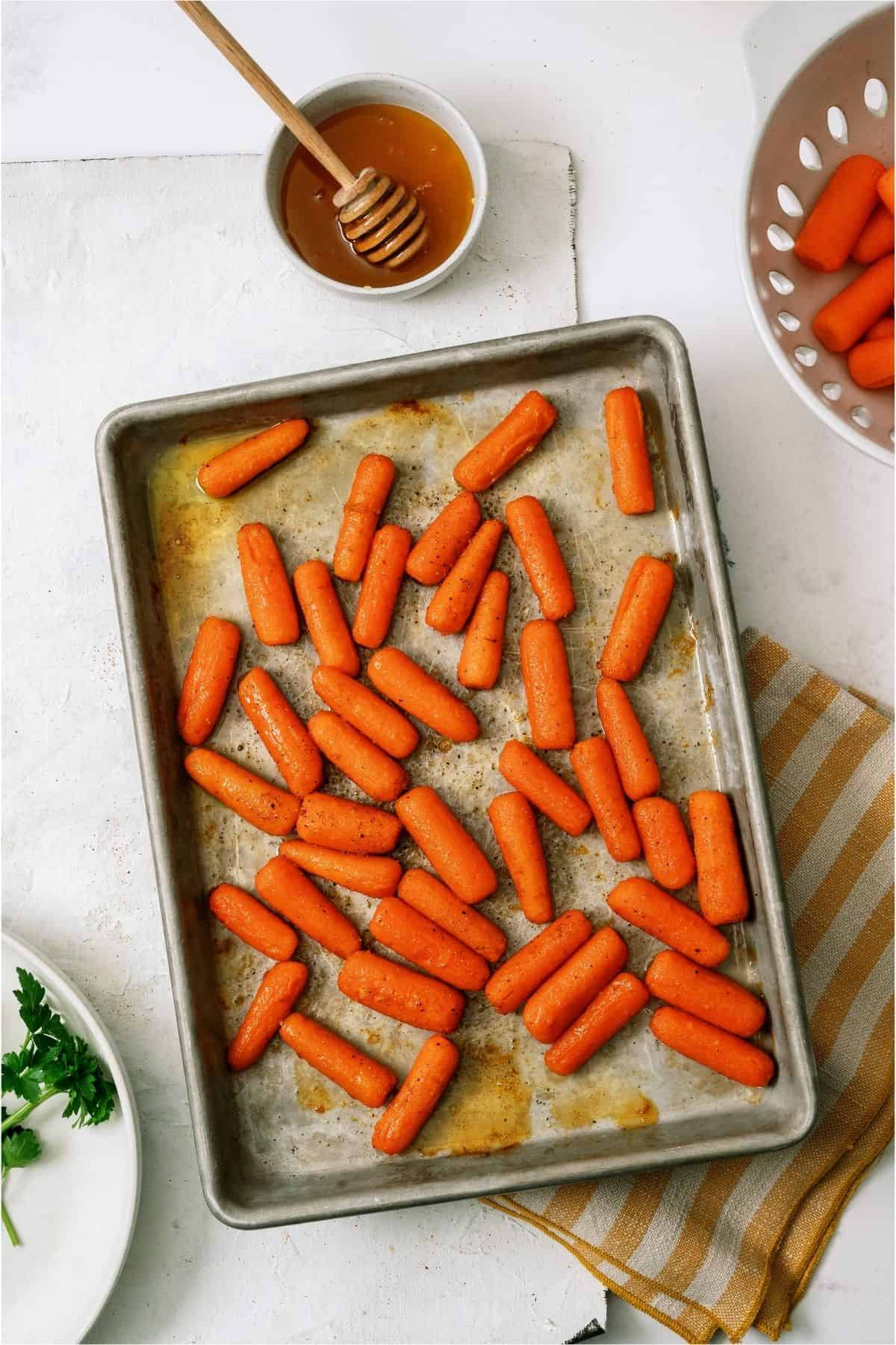 Baby carrots on a sheet pan with a honey pot next to it.
