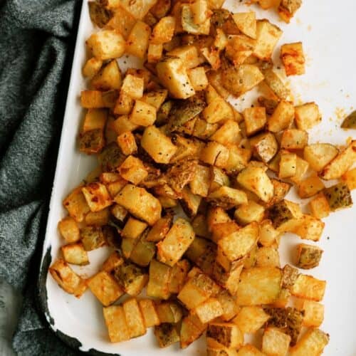 Diced, seasoned roasted potatoes spread on a white tray with a gray cloth underneath.