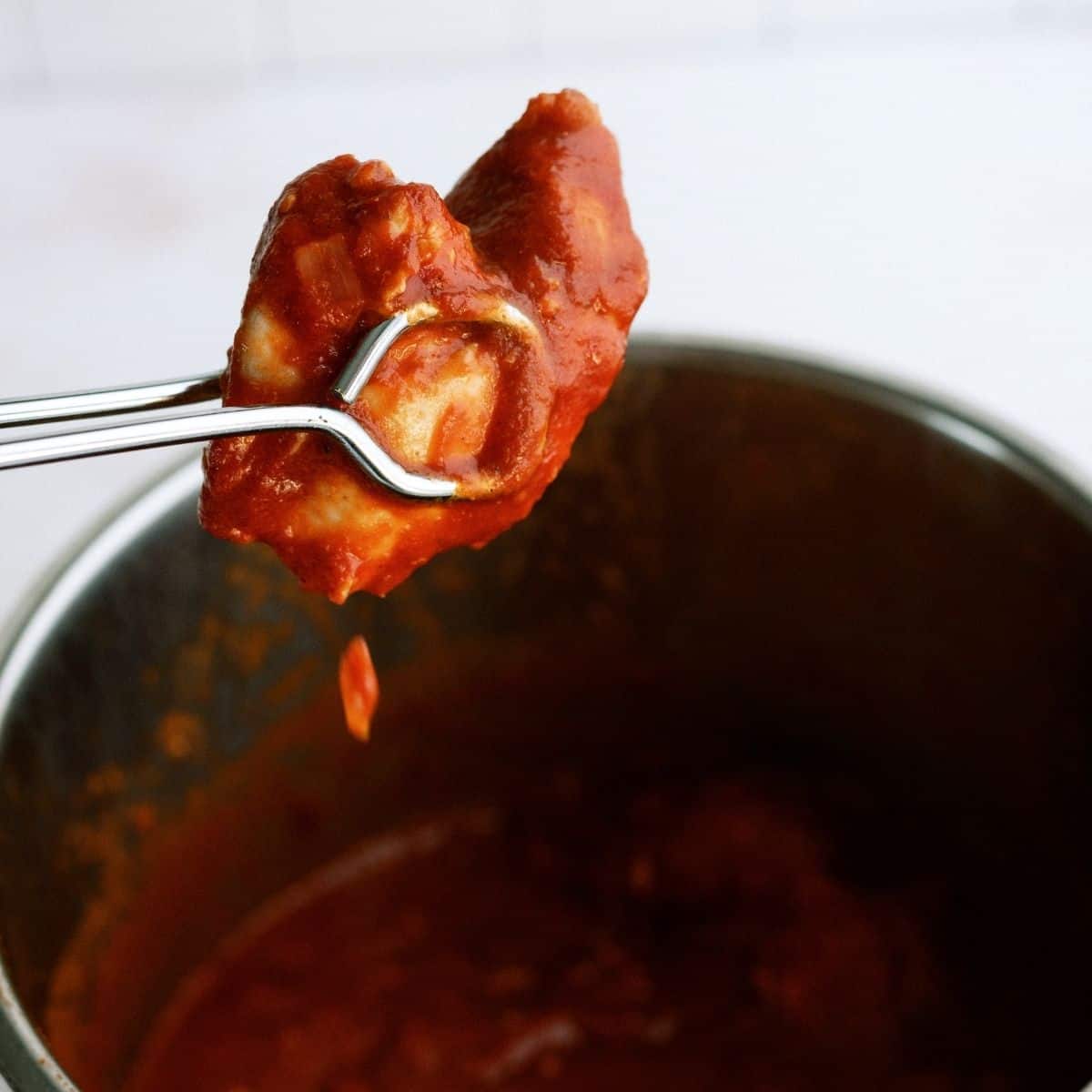 Instant Pot Butter Chicken in tongs