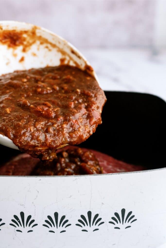 A thick, brown sauce is being poured from a white bowl into a white pot with black decorative patterns.