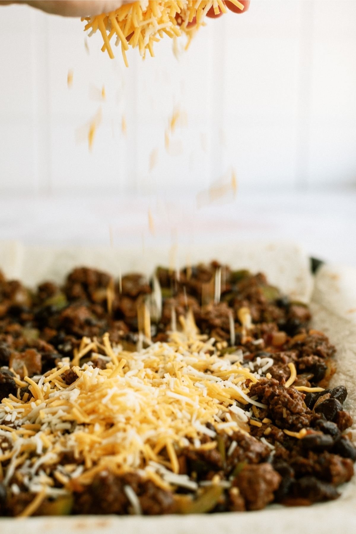 Shredded Cheese sprinkled over Meat mixture on top of tortillas for Sheet Pan Ground Beef Quesadillas Recipe