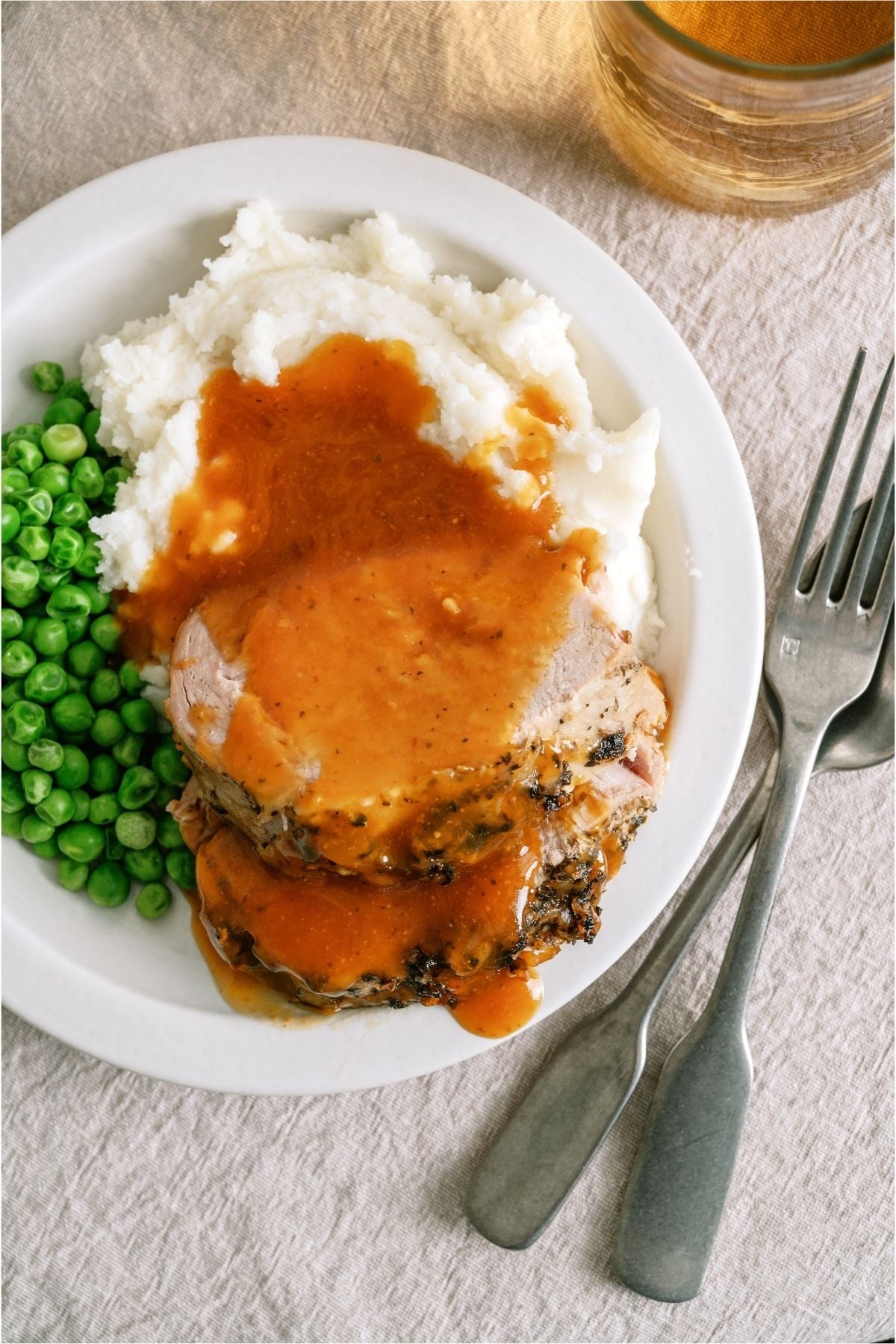 Top view of a plate with two slices of Slow Cooker Parmesan Honey Pork Roast, mashed potatoes, and peas.
