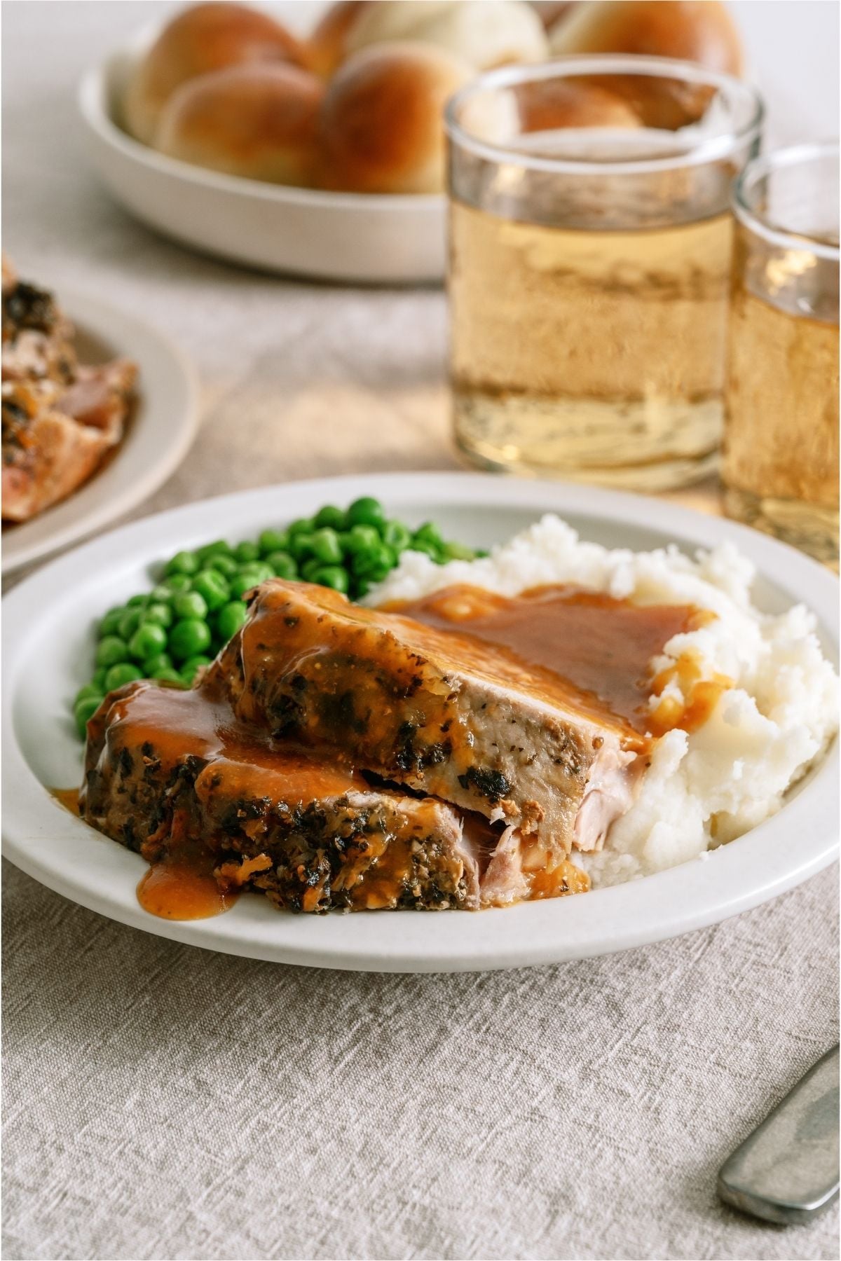A plate with 2 slices of Slow Cooker Parmesan Honey Pork Roast, mashed potatoes and peas.