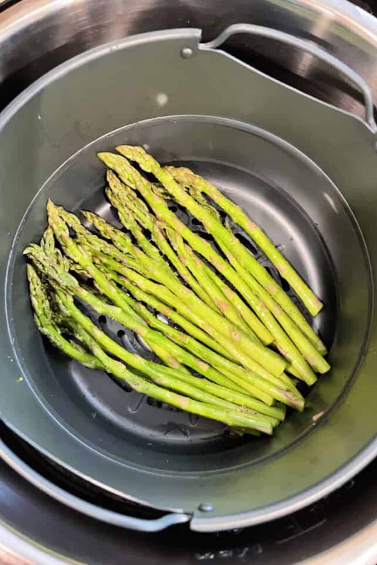 Seasoned and oiled asparagus in the bottom of an air fryer.
