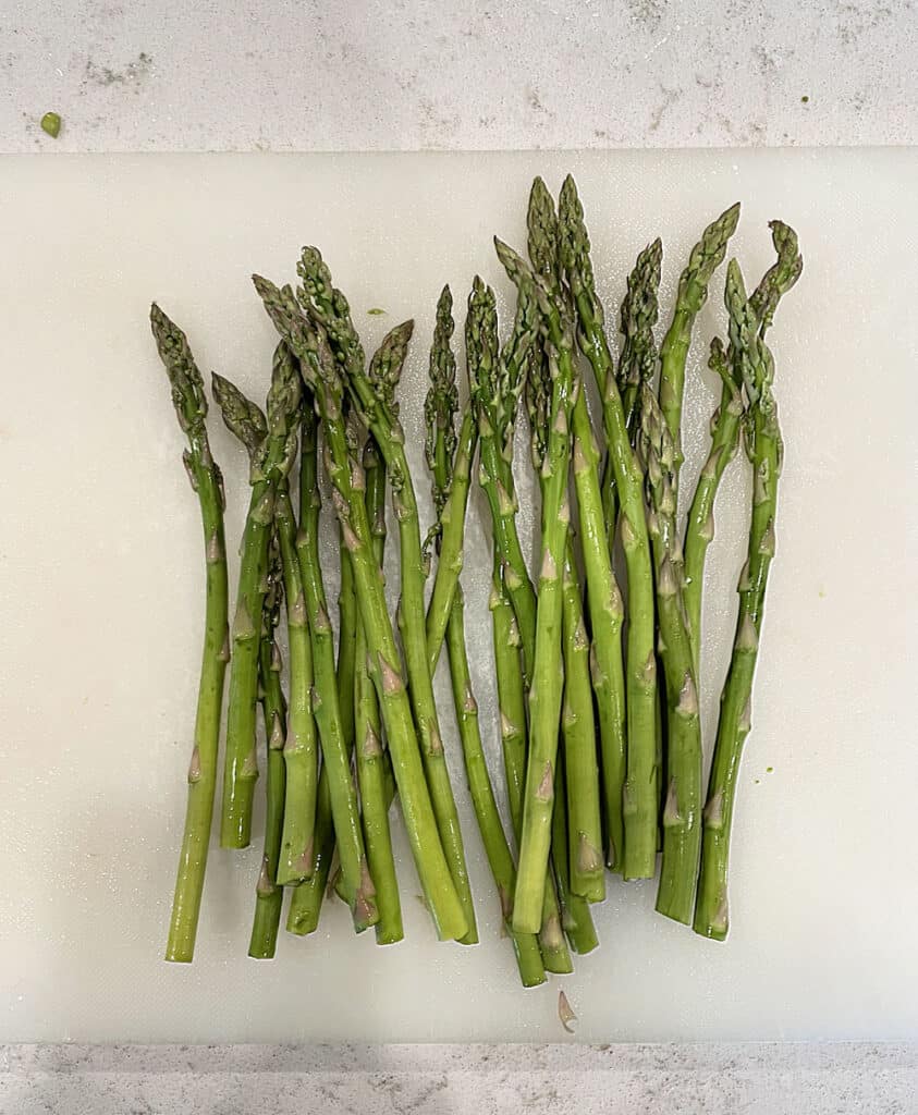 Fresh bunch of asparagus on a cutting board with the ends trimmed off.