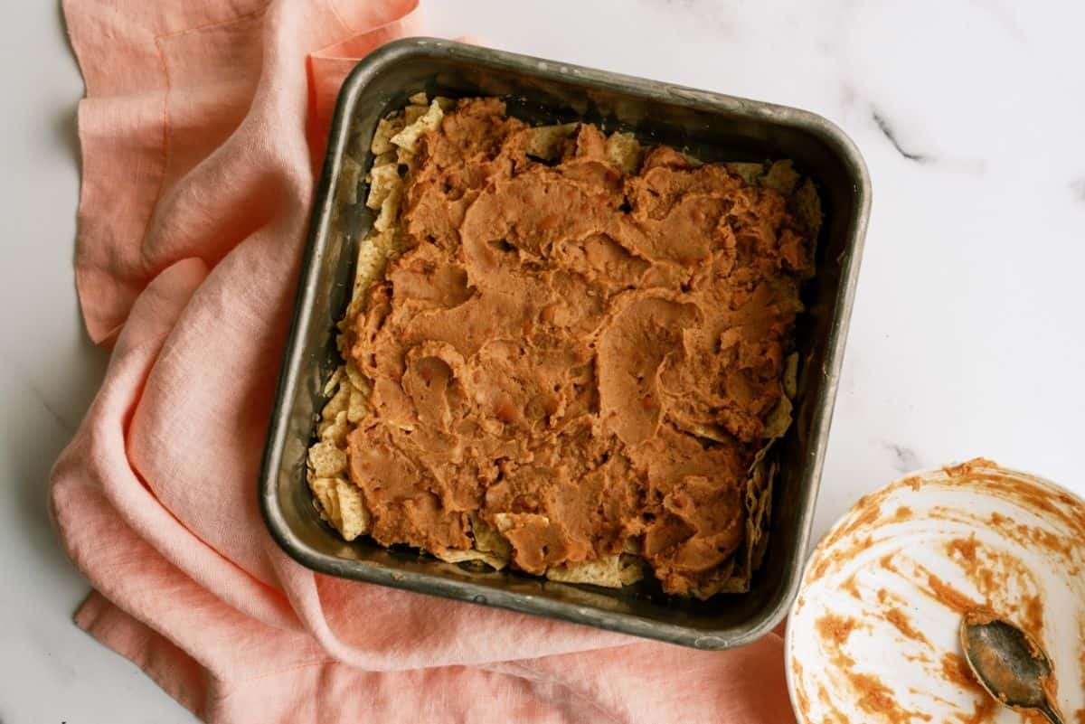 crushed tortillas topped with refried beans in an 8x8 pan