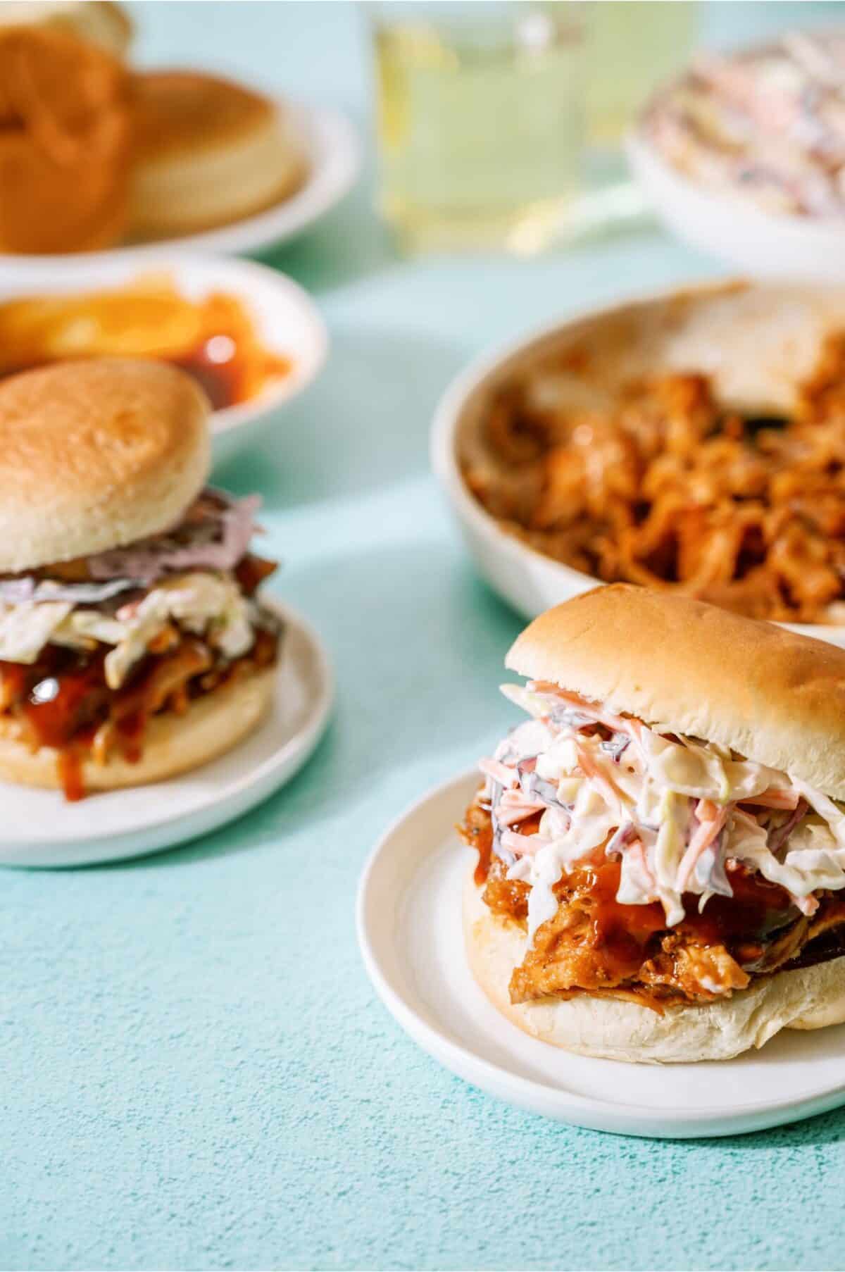 2 pulled pork sandwiches topped with coleslaw with a bowl of pulled pork in the background.