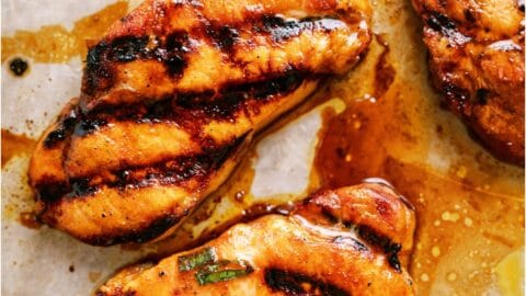 Grilled pork chops with visible char marks and marinade, arranged on a parchment-lined surface.