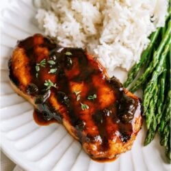 A plate with a grilled pork chop, rice and some asparagus.