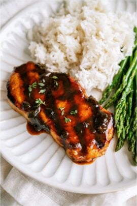 A plate with a grilled pork chop, rice and some asparagus.