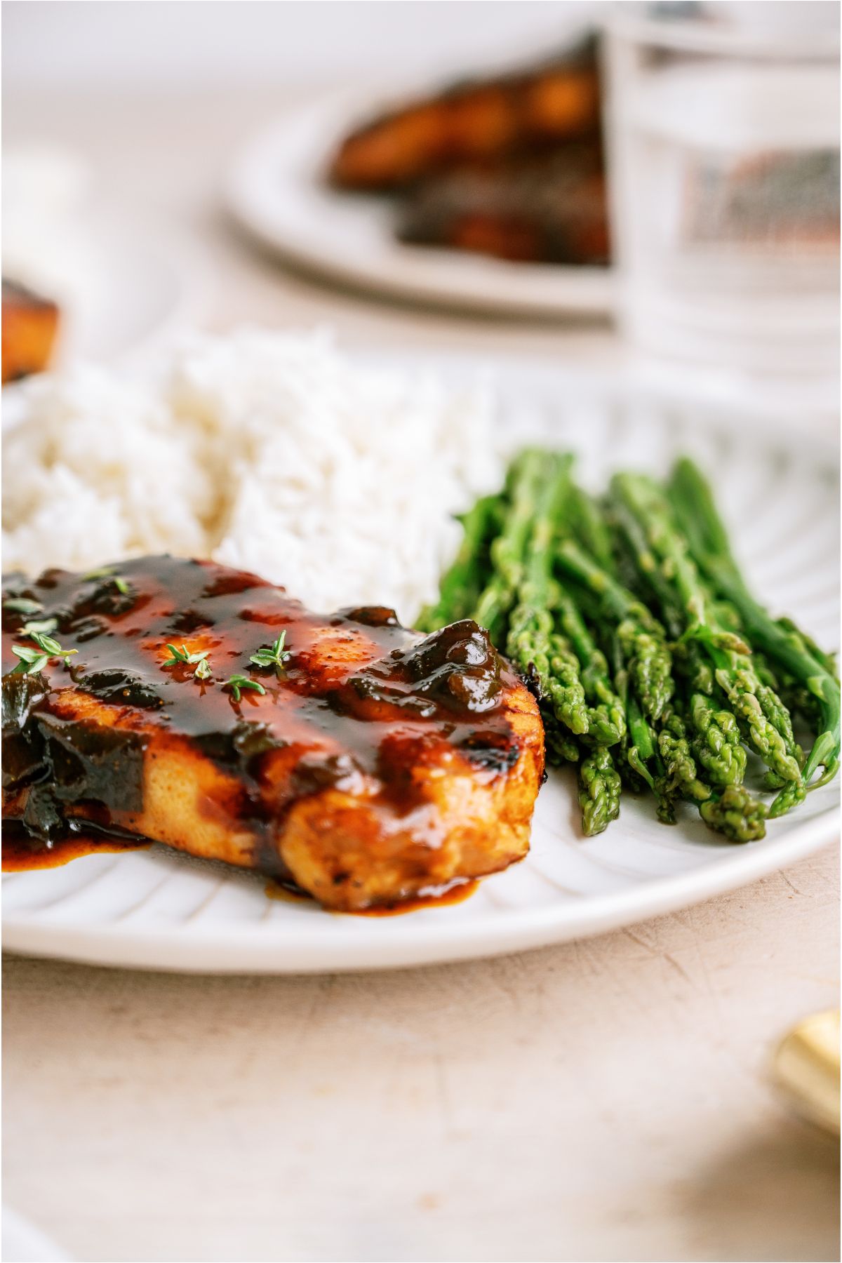 Side view of a marinated grilled pork chop on a plate with rice and asparagus.