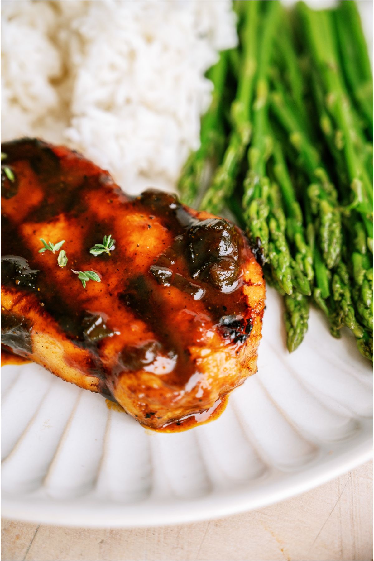 Top view of a marinated grilled pork chop on a plate with rice and asparagus.
