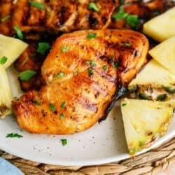 Top view of a piece of Grilled Huli Huli Chicken on a plate surrounded by slices of pineapple.