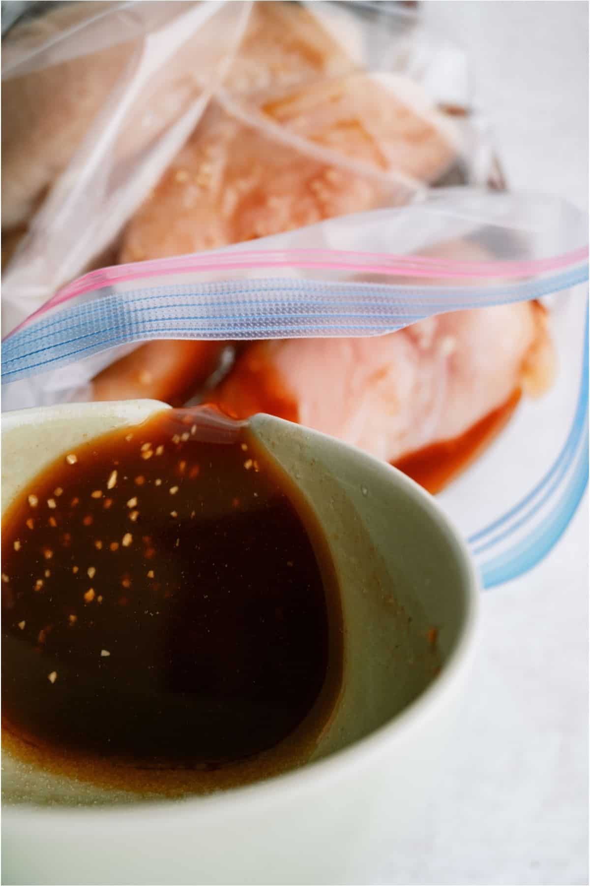Pouring Huli Huli marinade from a bowl into a ziploc bag of chicken breasts.