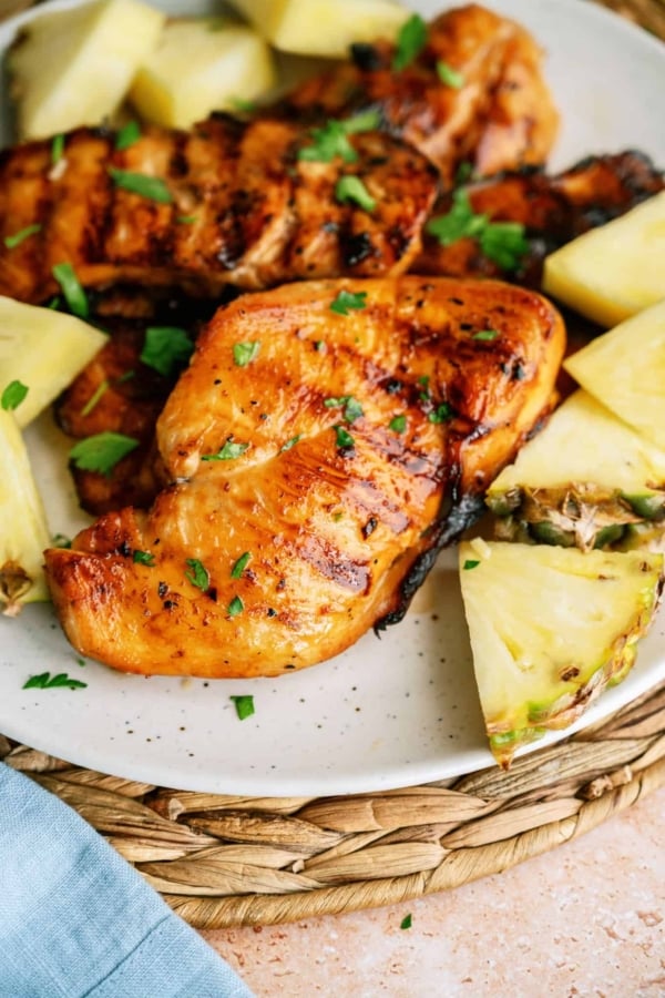 Top view of a piece of Grilled Huli Huli Chicken on a plate surrounded by slices of pineapple.