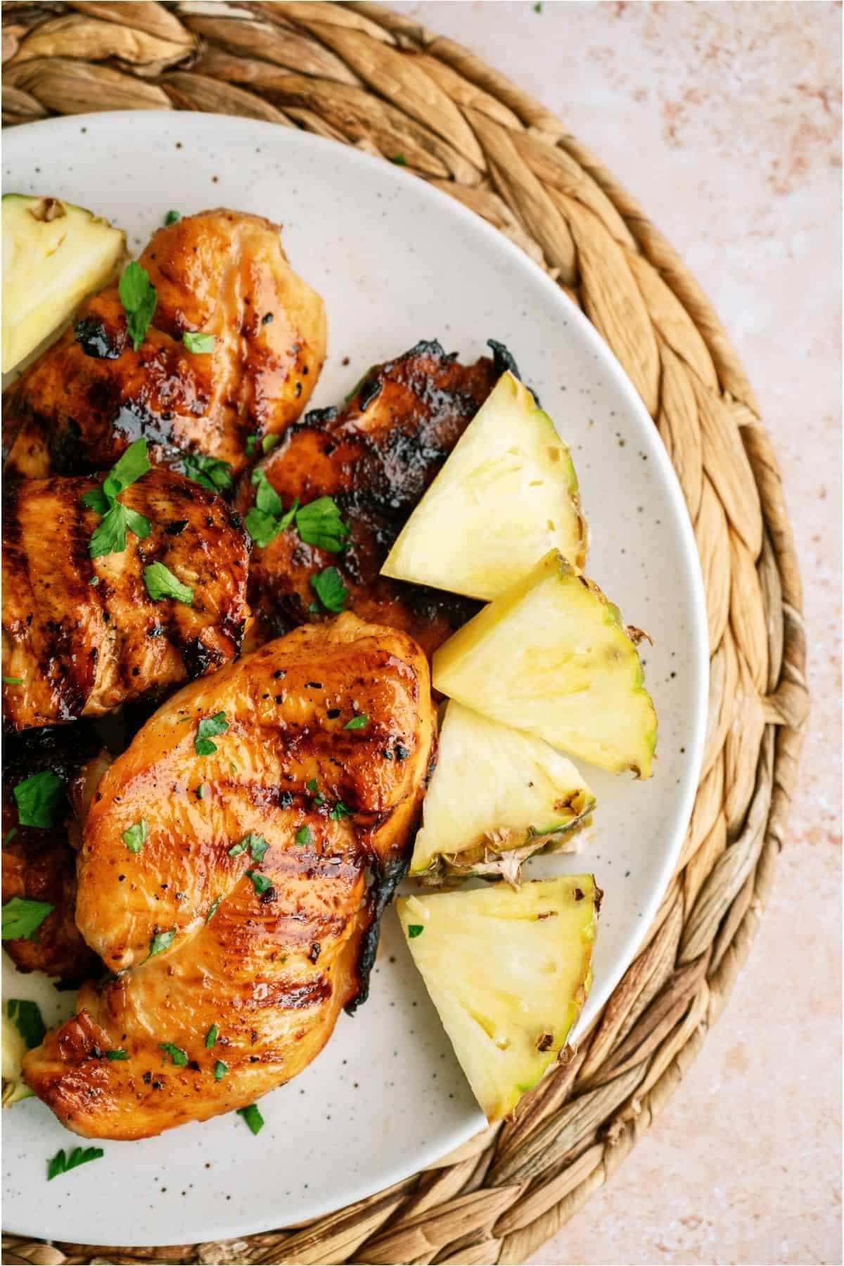 Top view of a plate of Grilled Huli Huli Chicken Breasts surrounded by slices of fresh pineapple.