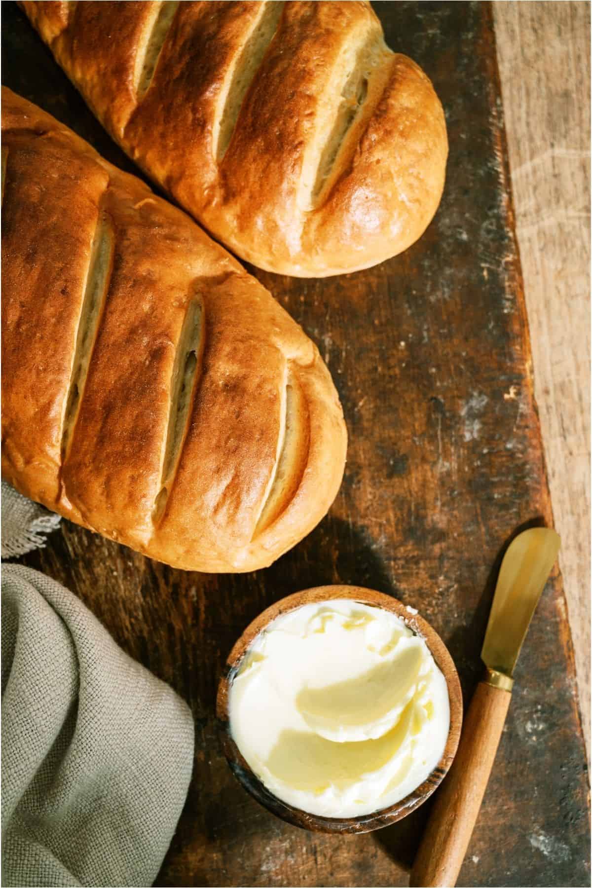 2 loaves of Homemade French Bread on a cutting board with a small dish of butter.