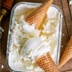 2 Ice Cream Cones with scoops on top of a container of Vanilla Ice Cream.