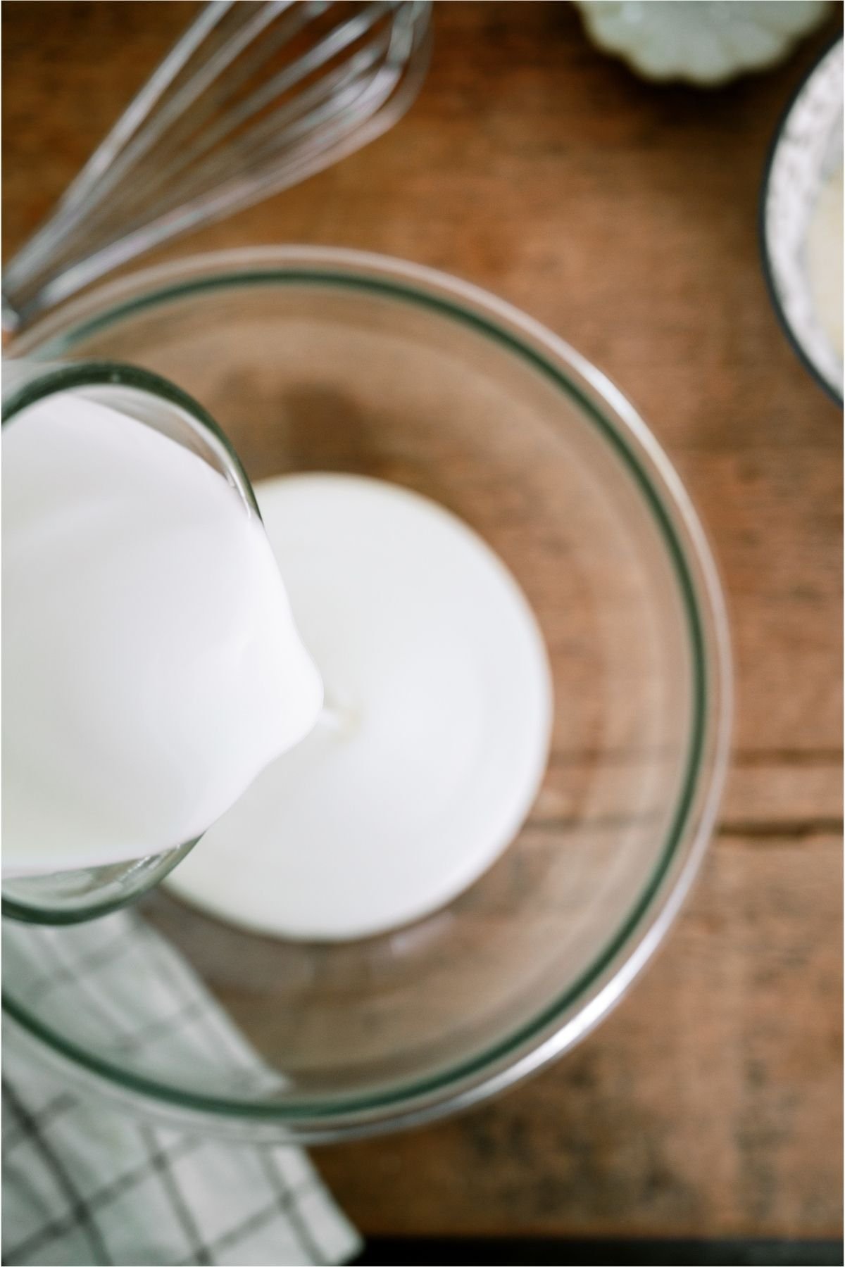 Pouring heavy cream into a glass mixing bowl.