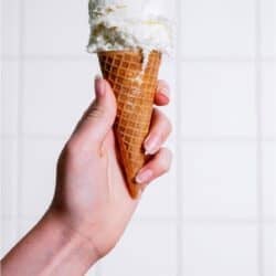 A hand holding a ice cream cone with a scoop of vanilla ice cream on top.