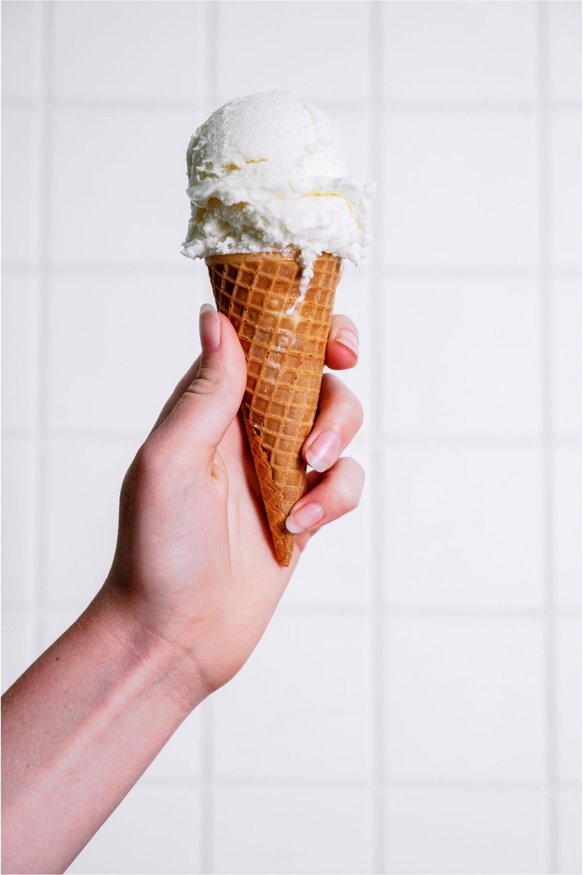 A hand holding a ice cream cone with a scoop of vanilla ice cream on top.