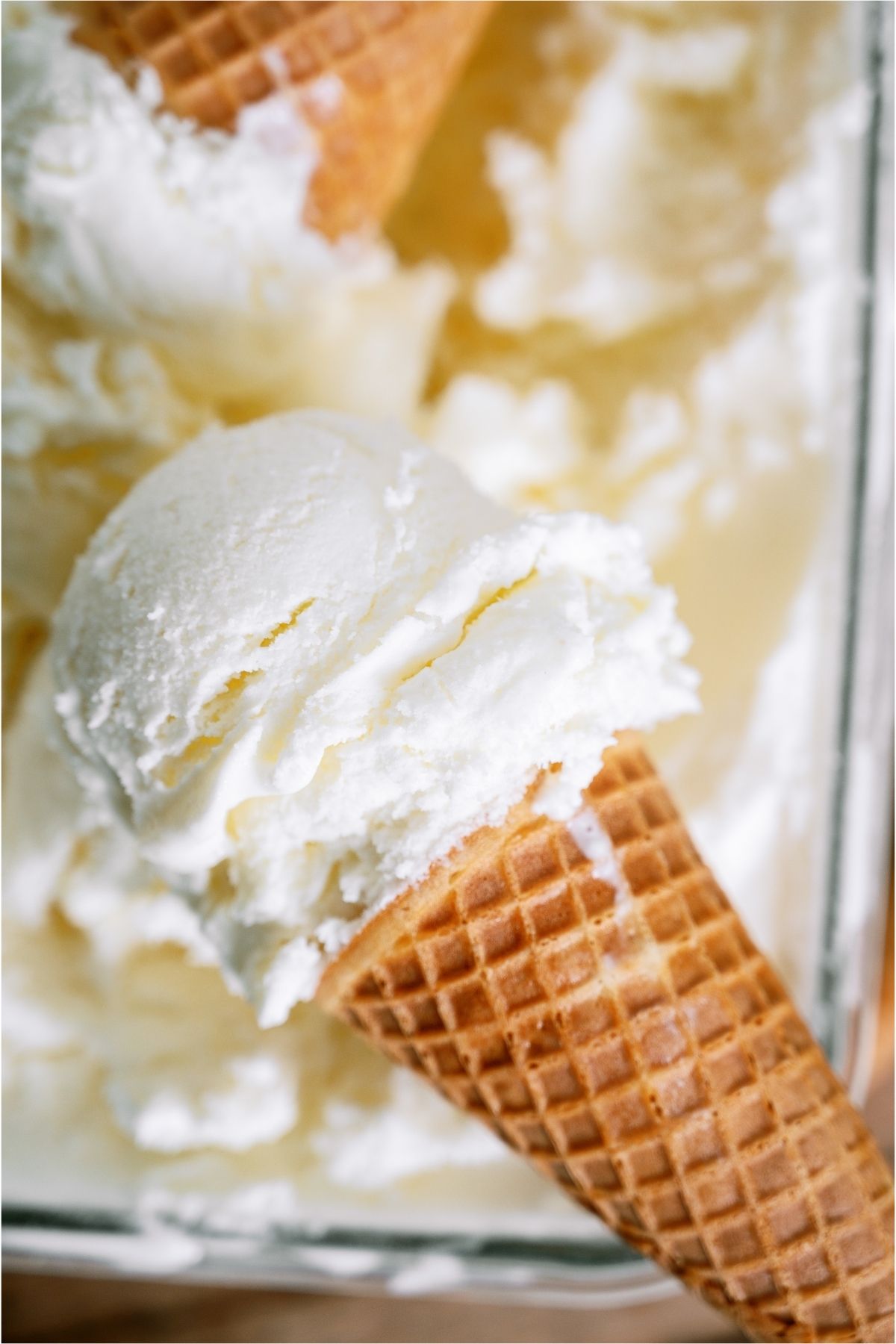 Close up of ice cream cone with a scoop of ice cream on top of an ice cream container.