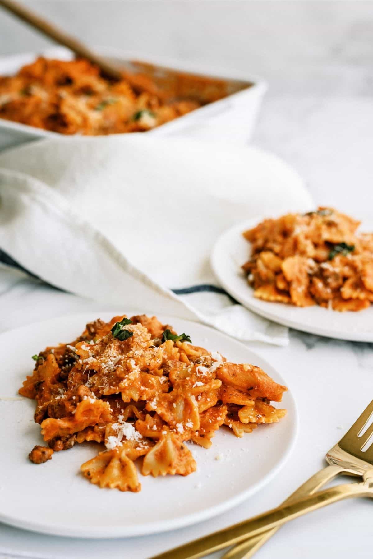 Instant Pot Ground Beef Lazy Lasagna in white casserole dish. Two white plates with servings of lasagna