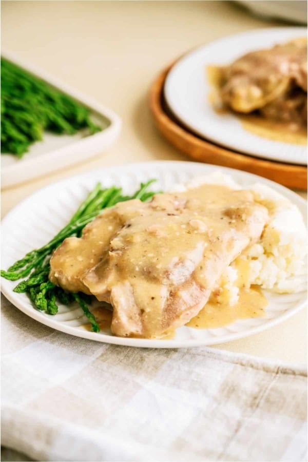 A white plate with Slow Cooker Pork Chops served over mashed potatoes with asparagus on the side.