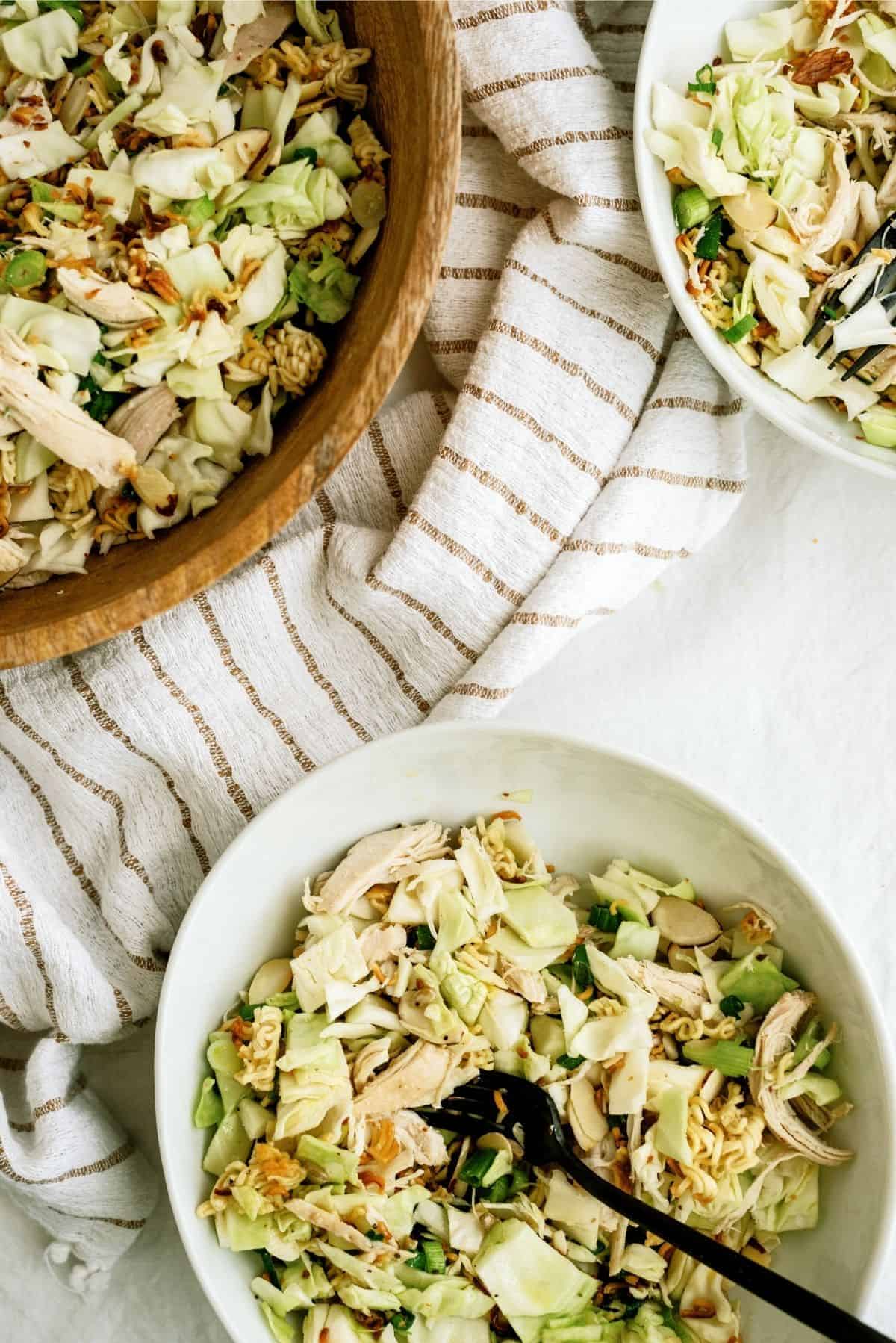 Bowls of salad featuring shredded cabbage, chicken, and crunchy toppings, with a striped cloth in the background.