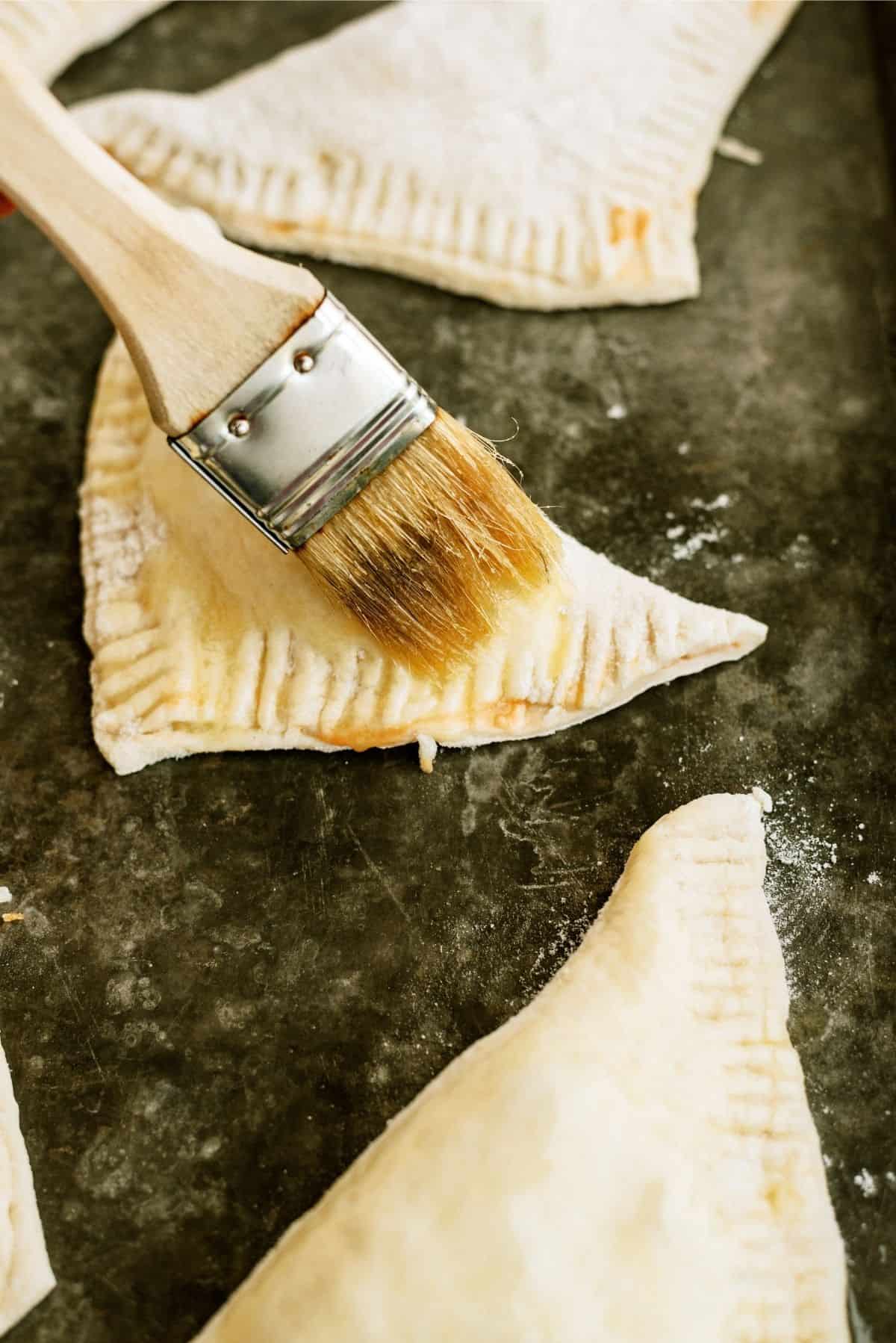 Brushing unbaked calzones with melted butter