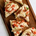 Five slices of pizza topped with melted cheese, chopped tomatoes, green onions, and bacon pieces on a wooden serving tray.