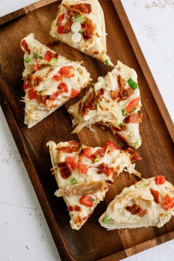Five slices of pizza topped with melted cheese, chopped tomatoes, green onions, and bacon pieces on a wooden serving tray.