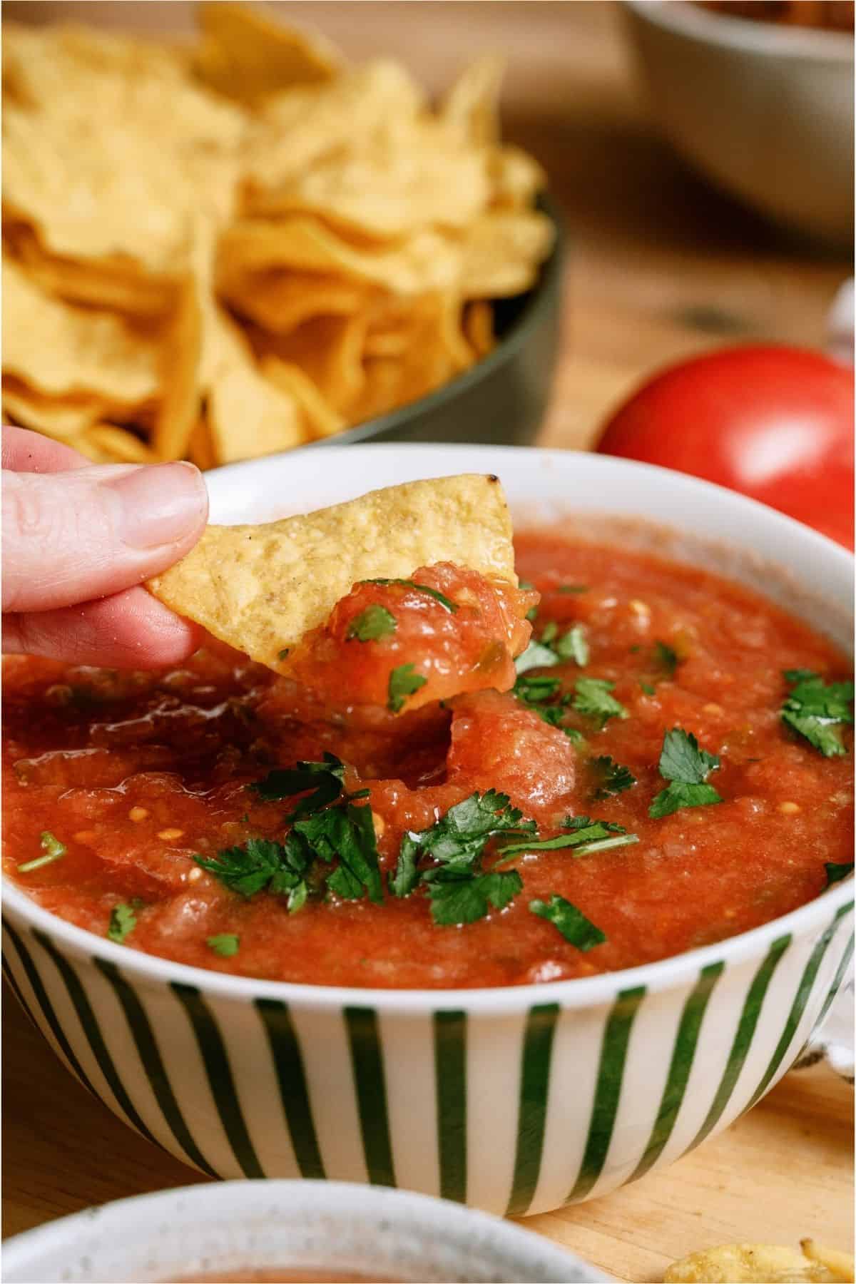 A hand dipping a chip in a bowl of Chili's Copycat Salsa.