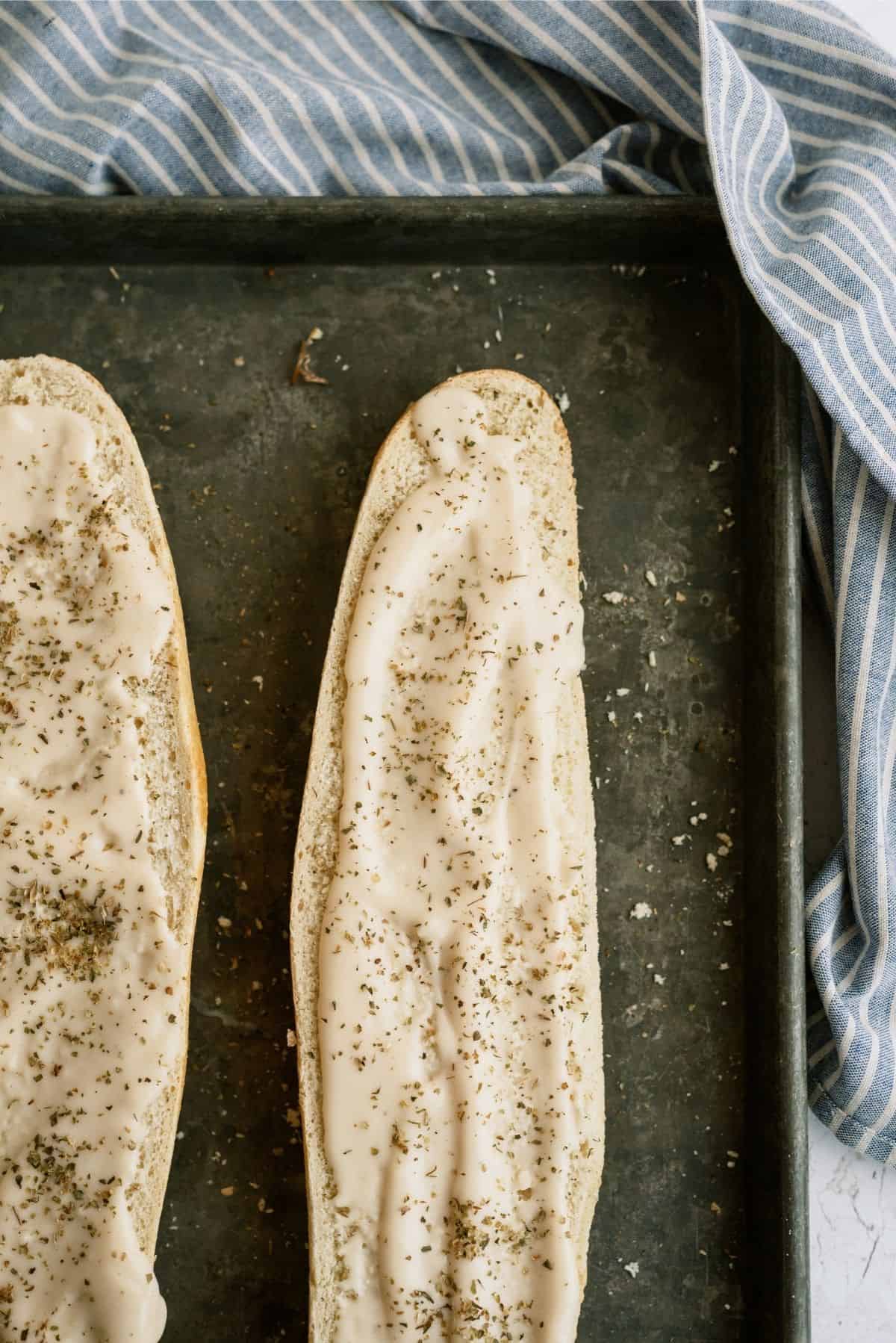 French Bread cut in half on a sheet pan with Alfredo sauce and seasoning