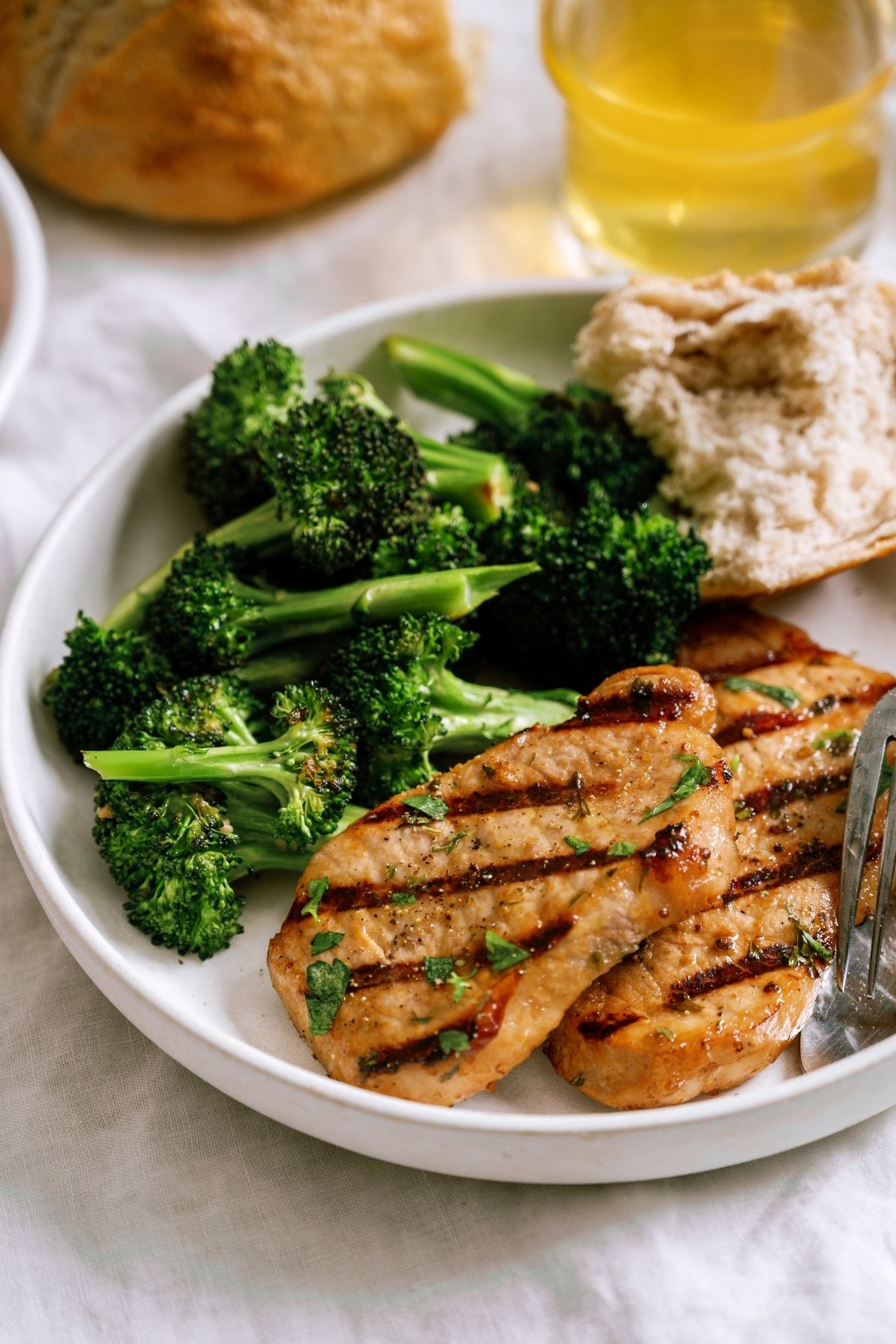 Marinated Grilled Pork Chop on a plate with a side of broccoli and a roll.