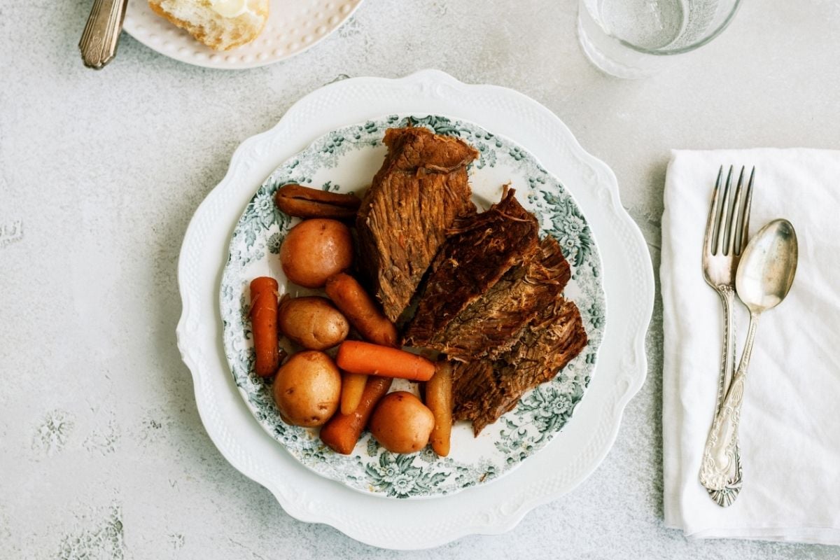 Melt In Your Mouth Slow Cooker Pot Roast on a white plate next to silverware
