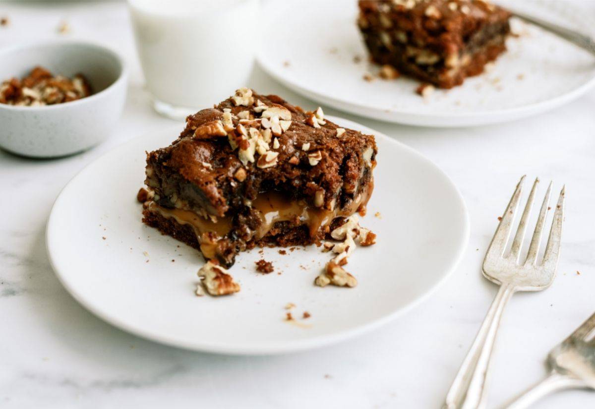 A slice of Snickers Cake on a plate with a bite missing to show the inside of the cake. A fork on the side.