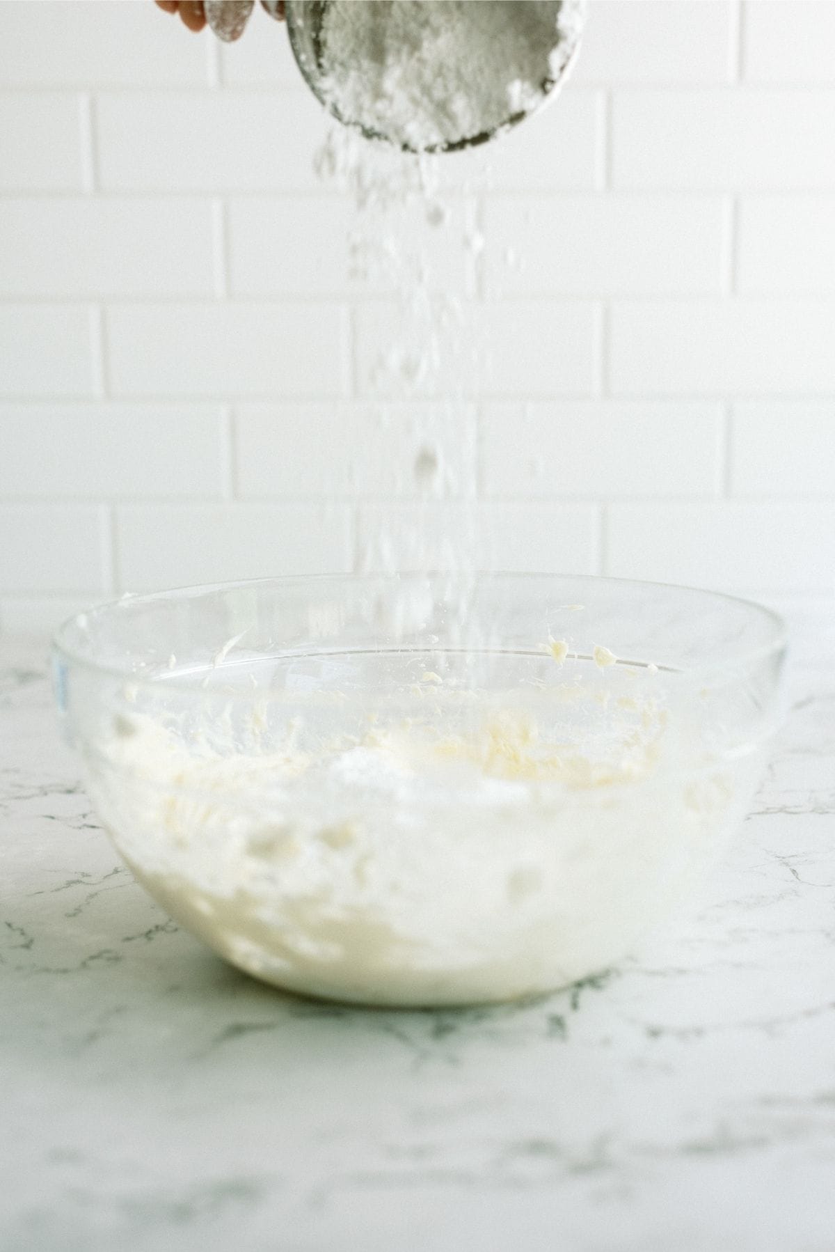 adding powdered sugar to cream cheese mixture in glass bowl