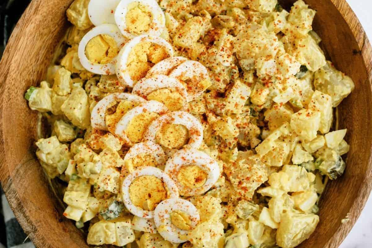 A bowl of potato salad topped with sliced hard-boiled eggs and sprinkled with paprika.