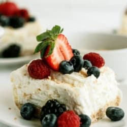 A slice of Fluffy Cream Cheese Dessert on a plate topped with berries.