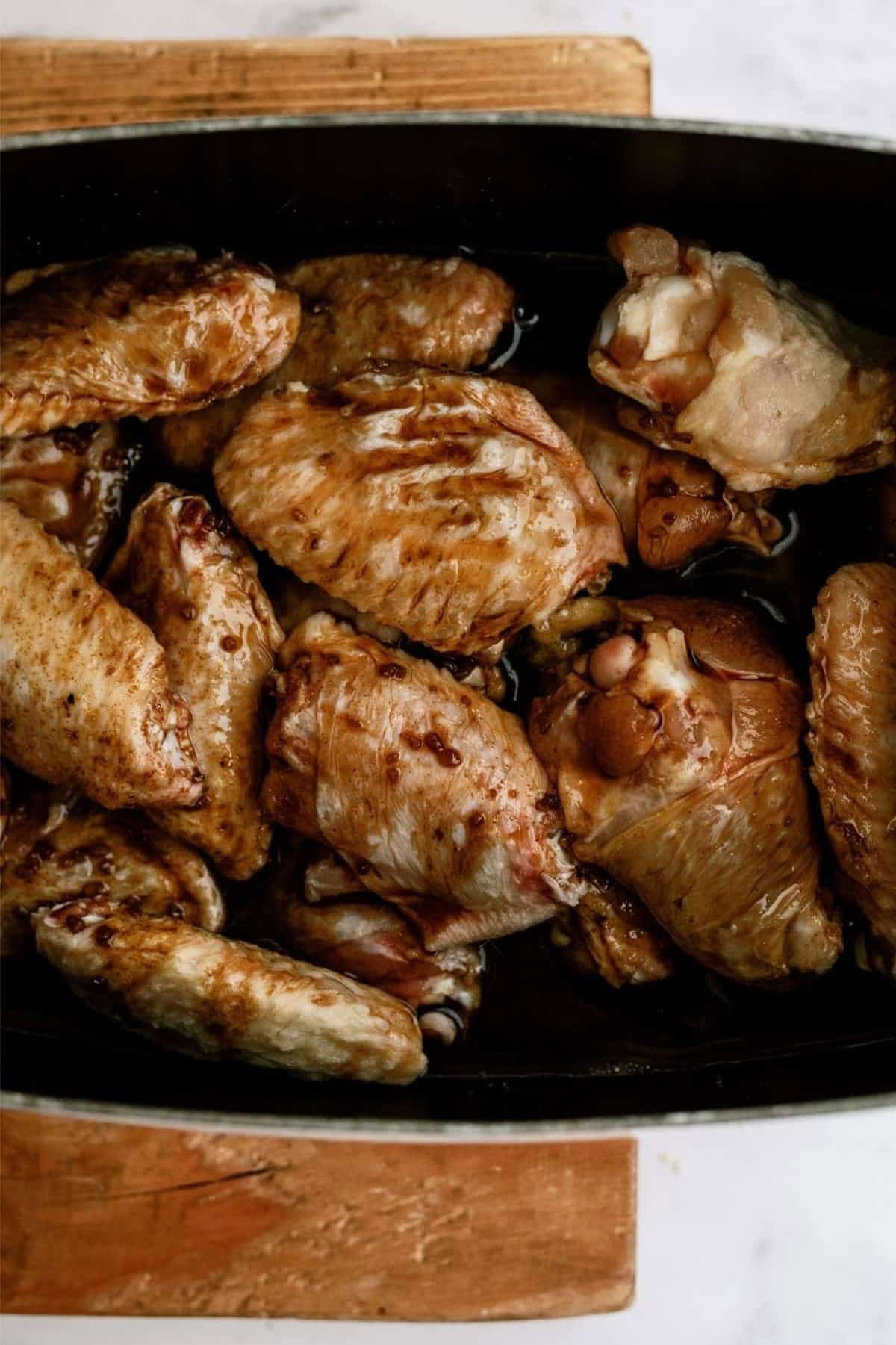 Cooked chicken wings in a black roasting pan on a wooden board.