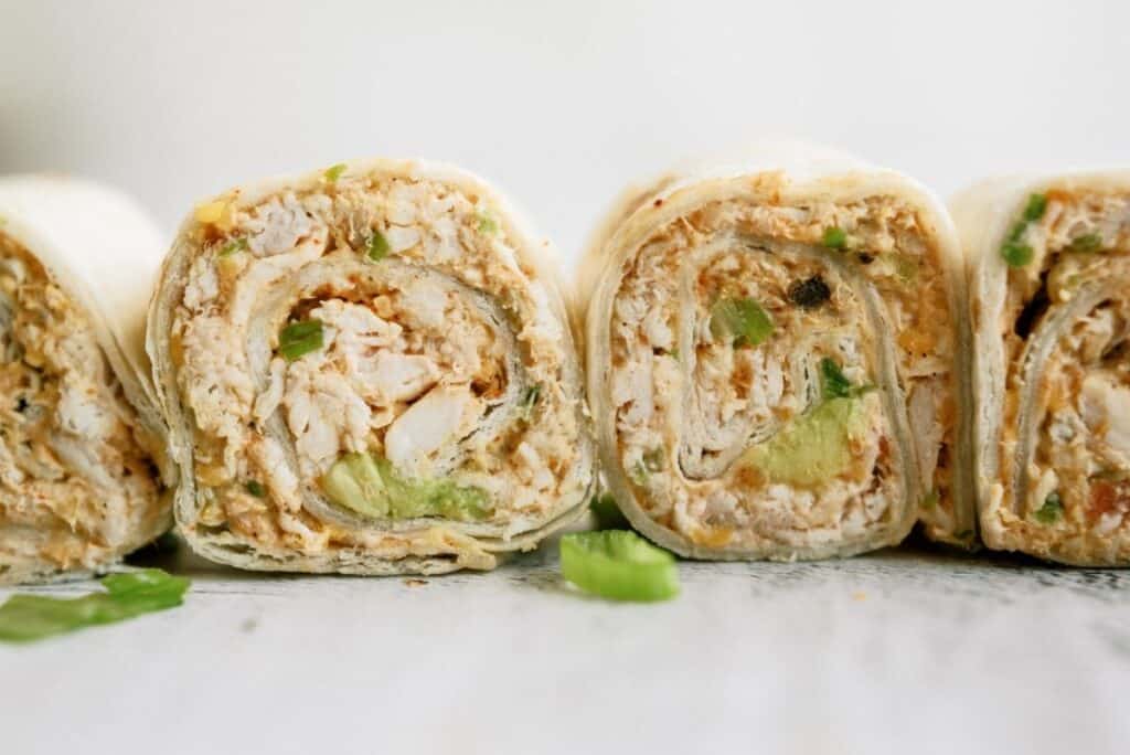 Close-up of sliced rolled tortillas filled with chicken, avocado, and herbs on a light surface.