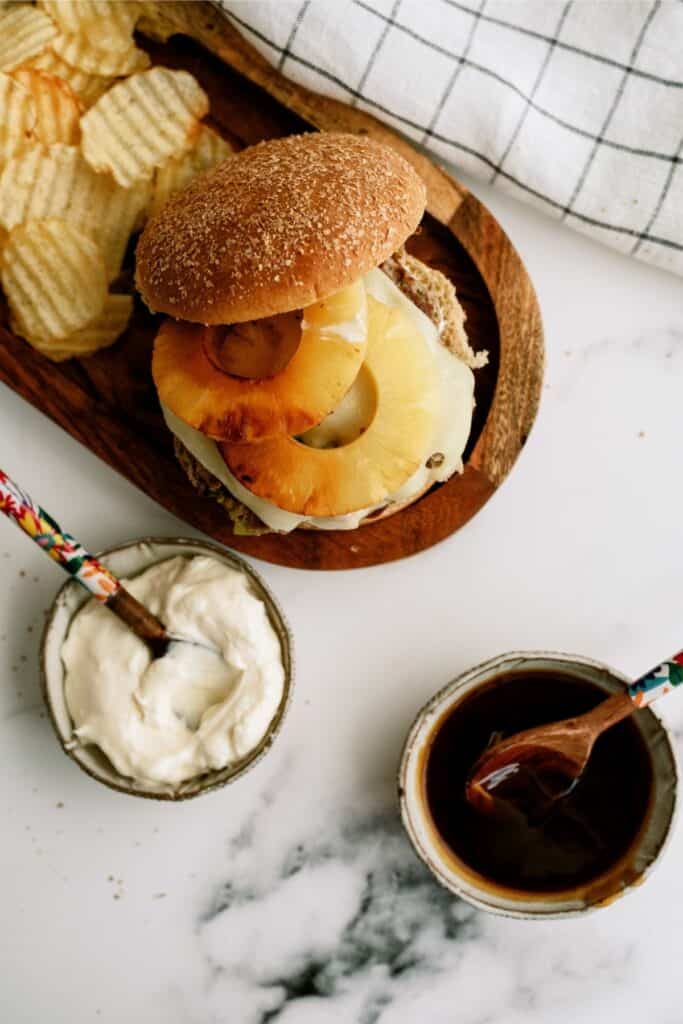 Hawaiian Turkey Burgers on a wooden plate with small bowls of sauce.