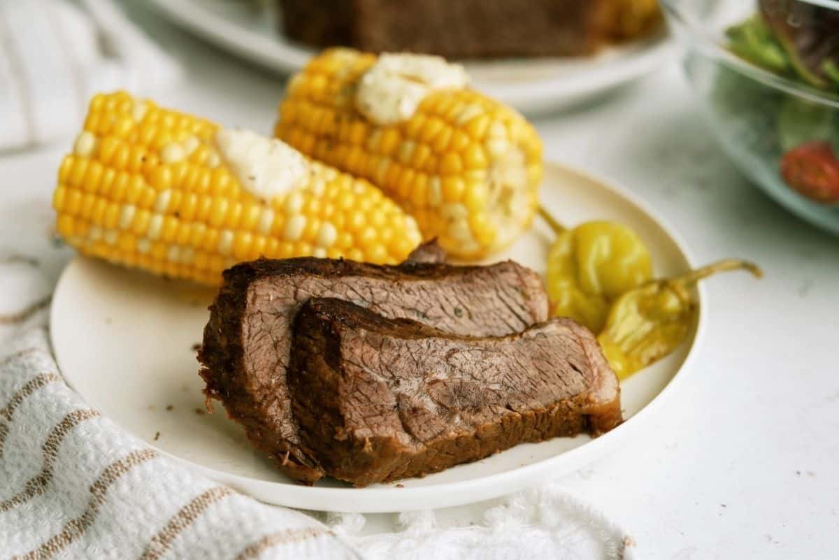 Instant Pot Mississippi Pot Roast sliced on a white plate with corn on the cob and pepperoncini peppers