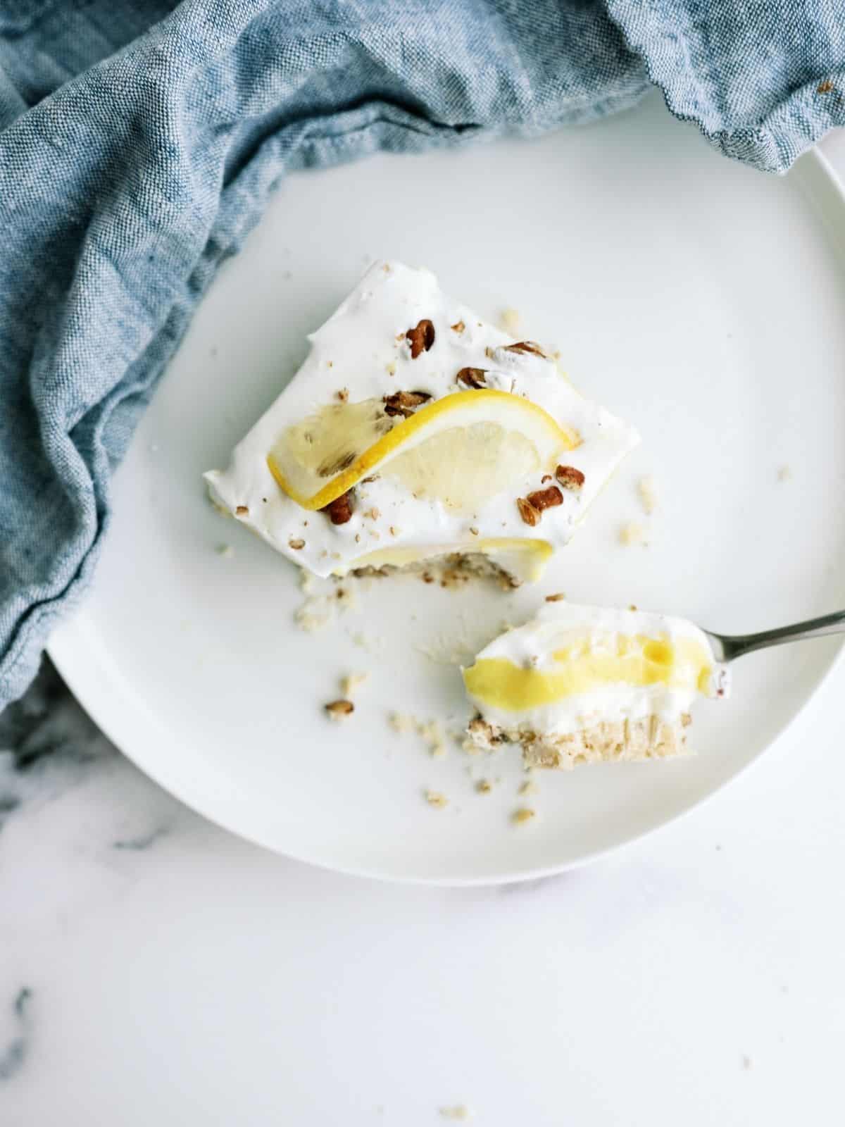 A slice of Layered Lemon Dessert on a white dish with a fork