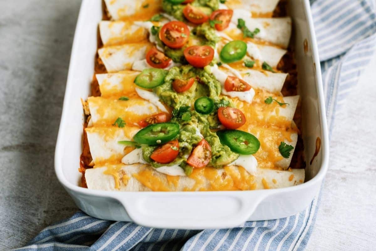 Slow Cooker Ranch Chicken Enchiladas in white baking dish topped with peppers, tomatoes and guacamole