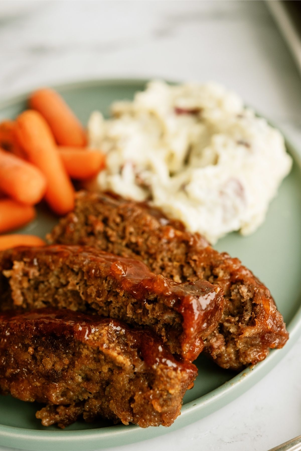 Sweet and Tangy Meatloaf with mashed potatoes and carrots on a green plate