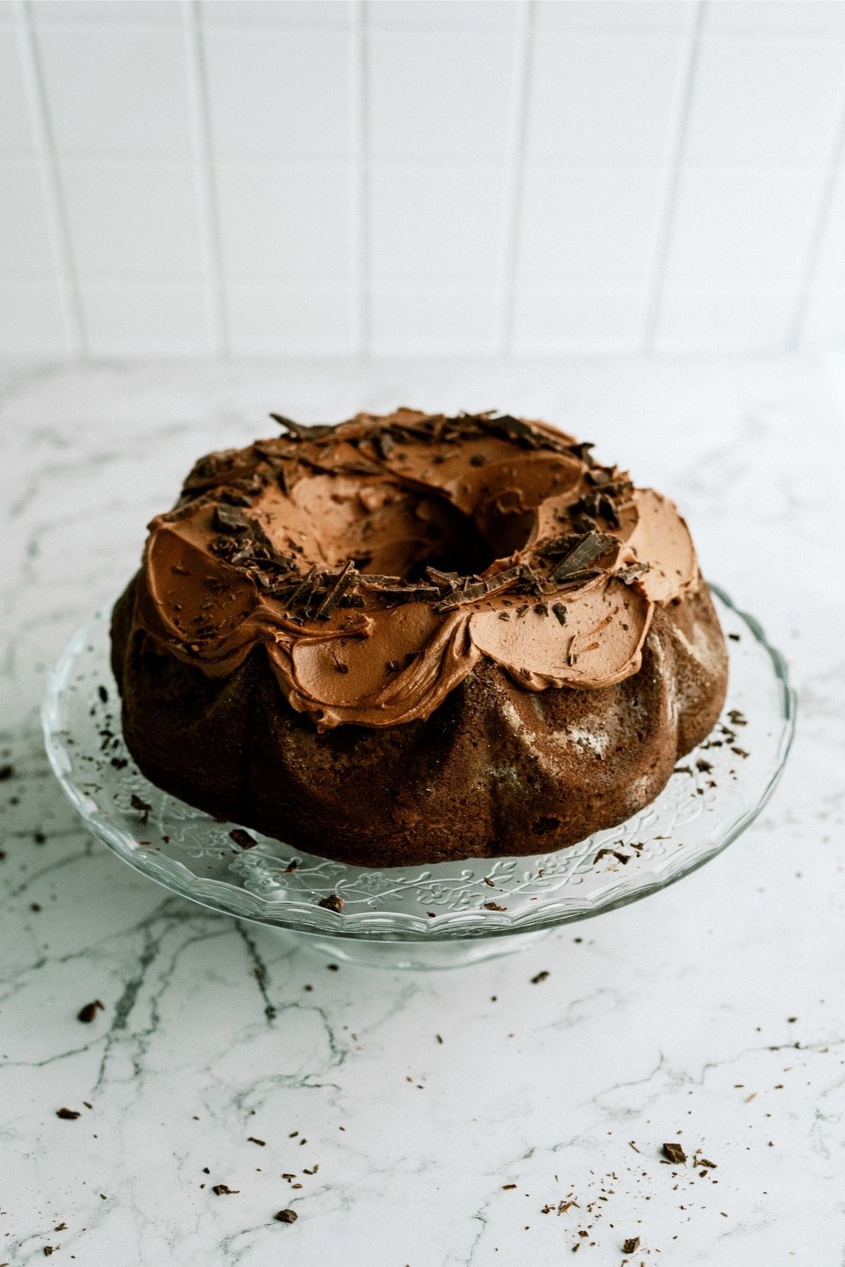 Triple Chocolate Bundt Cake on a glass cake stand with chocolate shavings